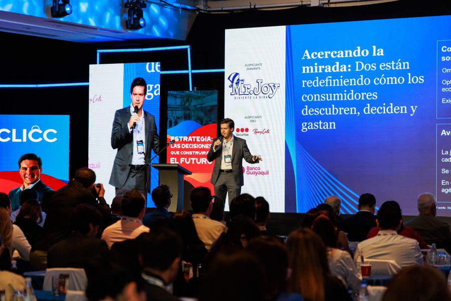 Speaker presenting on a lit stage before a full plenary audience at a business congress