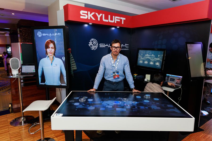 Exhibitor at a tech booth with interactive touch table and digital avatar screen