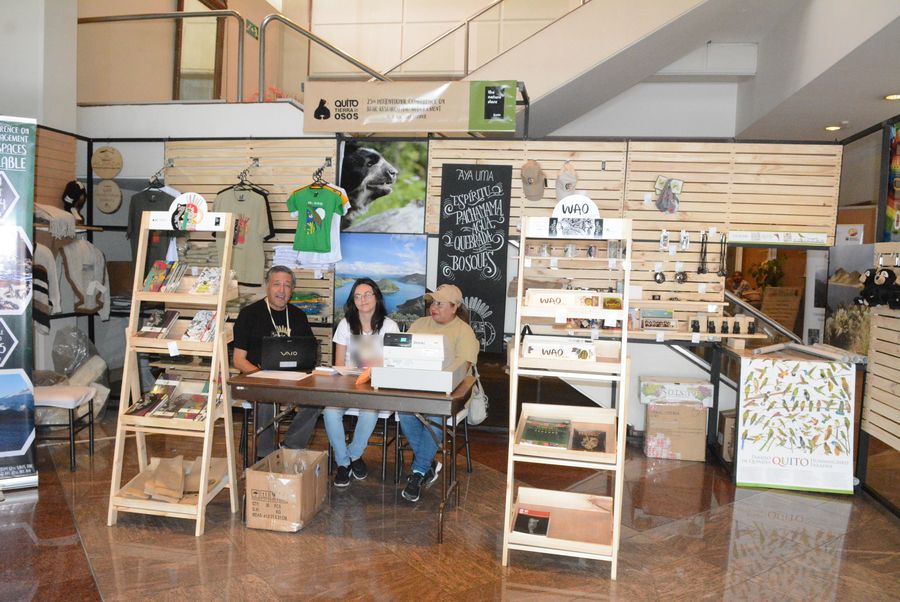 Conference merchandise booth with wooden shelves, T-shirts, books and Ecuadorian crafts