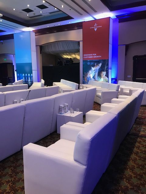 Rows of white lounge sofas and side tables set up for a corporate forum