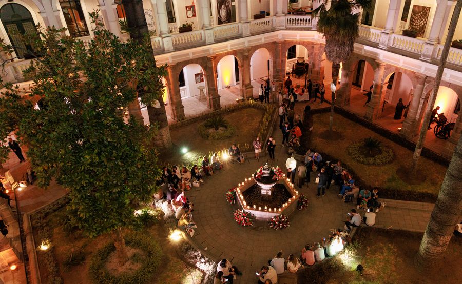 Aerial night view of a cocktail reception in a colonial courtyard, with a candlelit rose-decked fountain and guests gathered around