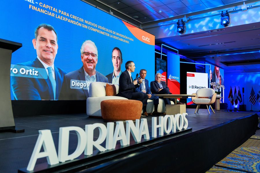 Three executives in a panel discussion on a modern stage with large LED screens