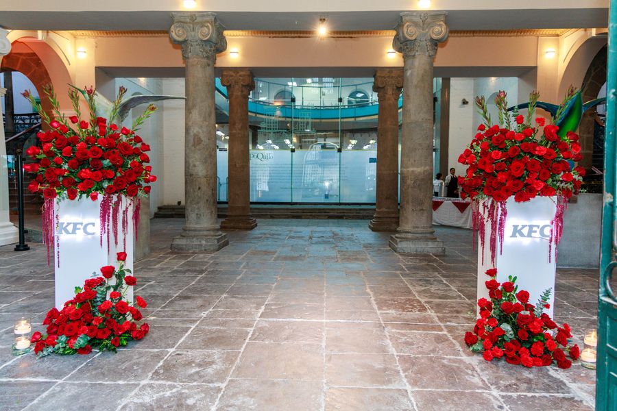 Entrance to a colonial courtyard framed by tall red rose arrangements on white pedestals