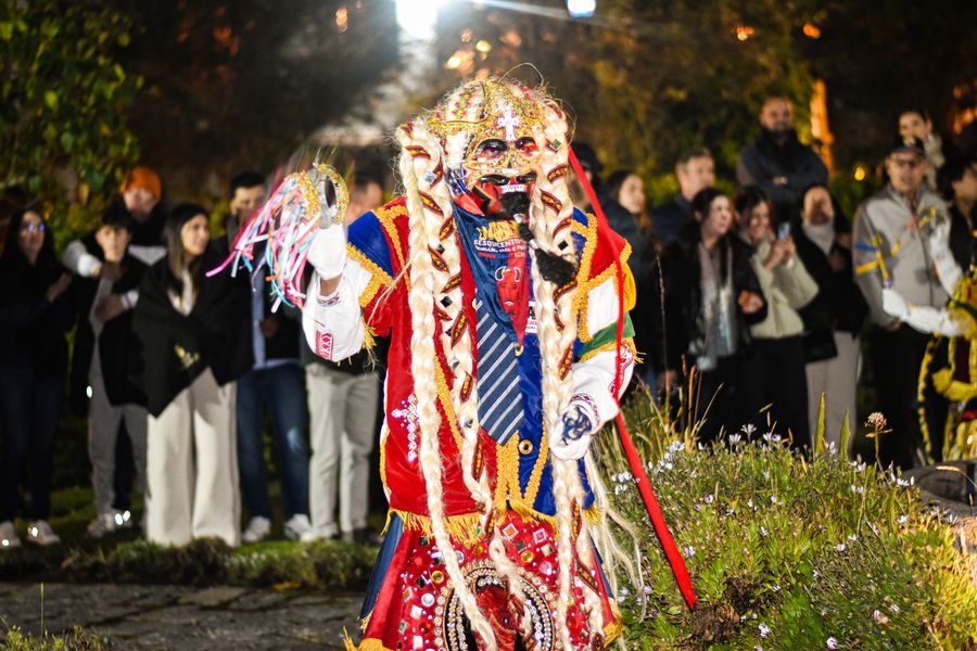 Masked Andean devil dancer in a red and gold costume performing for guests at an evening garden celebration