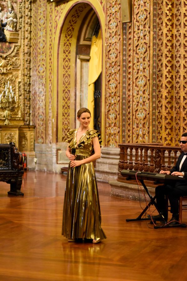 Singer in a golden gown performing beside a keyboard player inside an ornate gilded colonial church