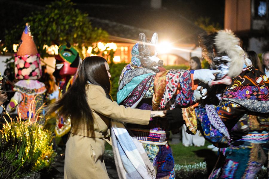 Guest joining hands with colorful masked folk dancers during a festive night celebration in a garden