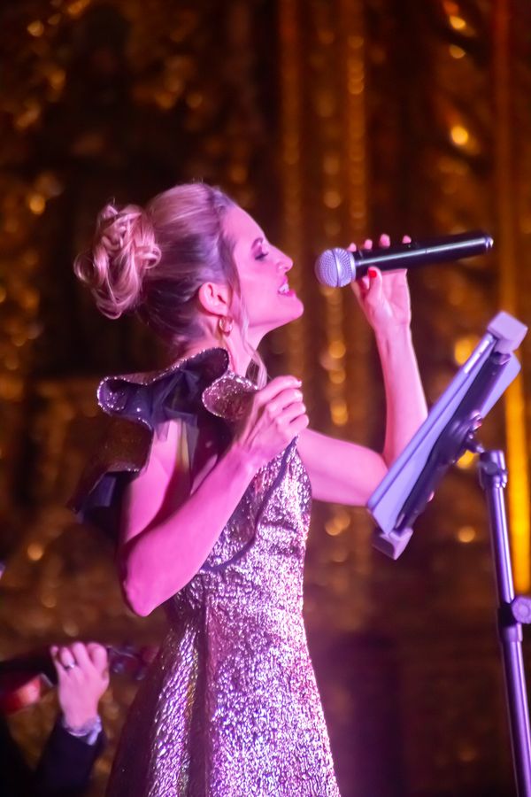 Singer in profile with eyes closed performing into a microphone under warm golden stage lights