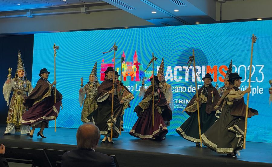 Folk dancers in Andean costumes and masked characters with staffs performing on a conference stage