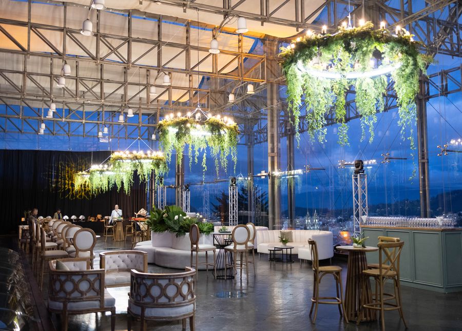 Glass-walled cocktail lounge with hanging greenery chandeliers overlooking the city at blue hour