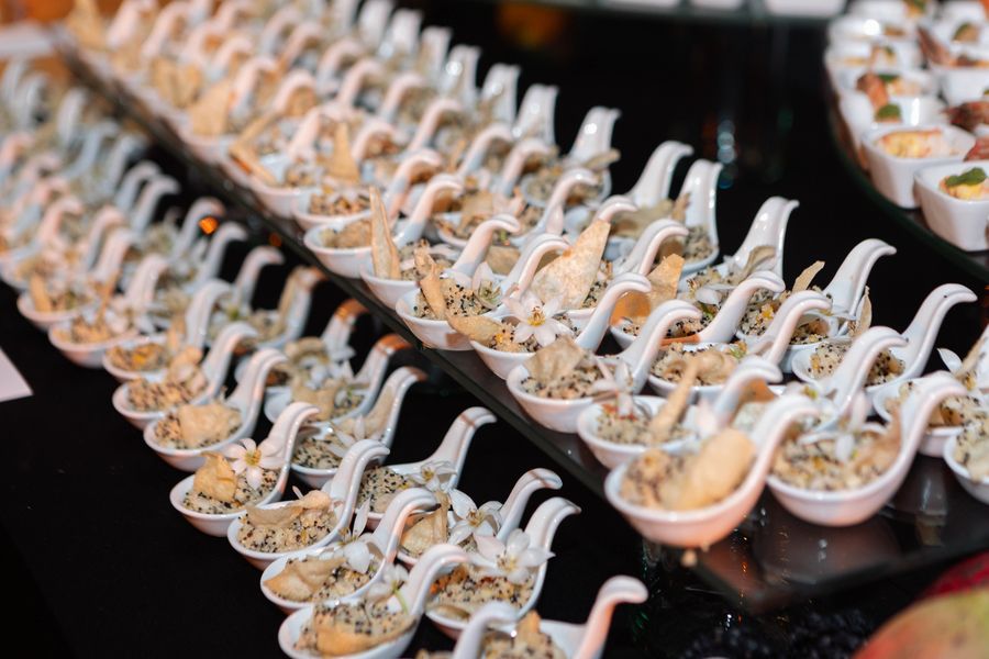 Rows of quinoa canapés with crispy wafers on white porcelain spoons, garnished with delicate white flowers