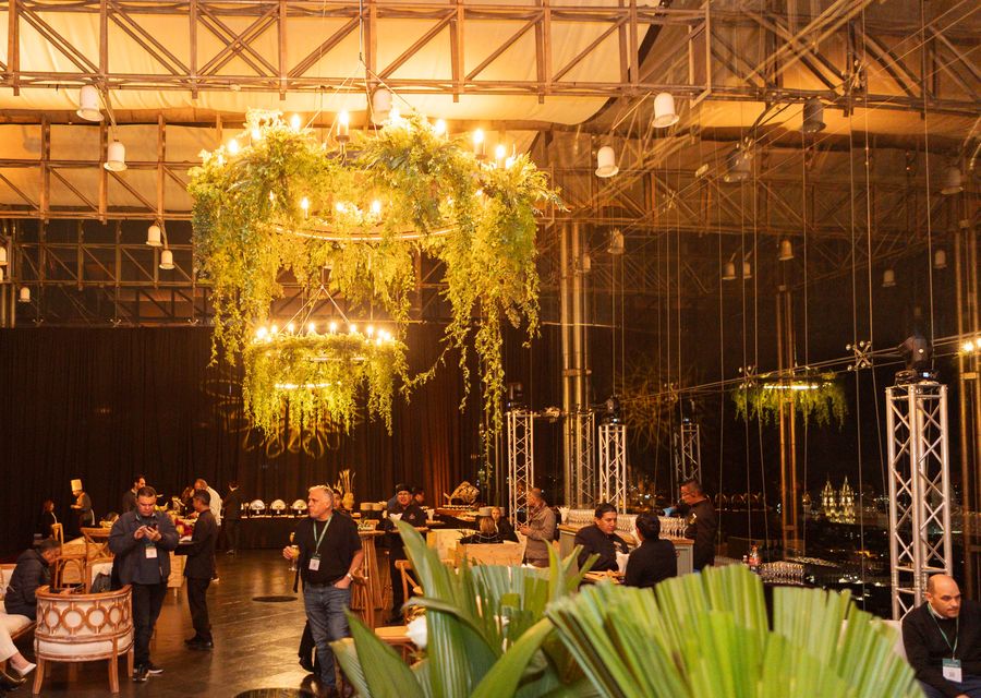 Cocktail reception in full swing under candlelit greenery chandeliers, with guests, bar staff and the illuminated basilica beyond the windows