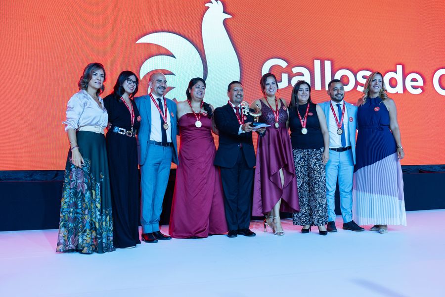 Large team with medals and a golden trophy posing on stage at an awards gala