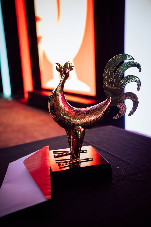Metallic rooster trophy on a dark table glowing under red and orange stage lights