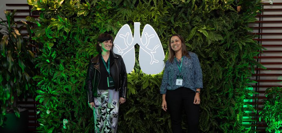 Two guests smiling at a lush living green wall photocall with an illuminated lung-shaped sign