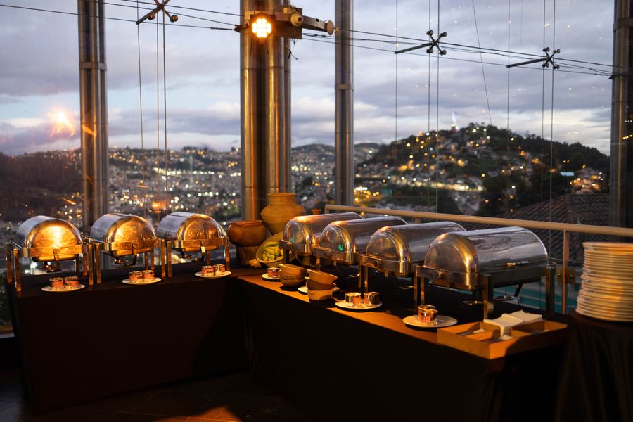 Rows of polished chafing dishes on a buffet overlooking the illuminated city at dusk