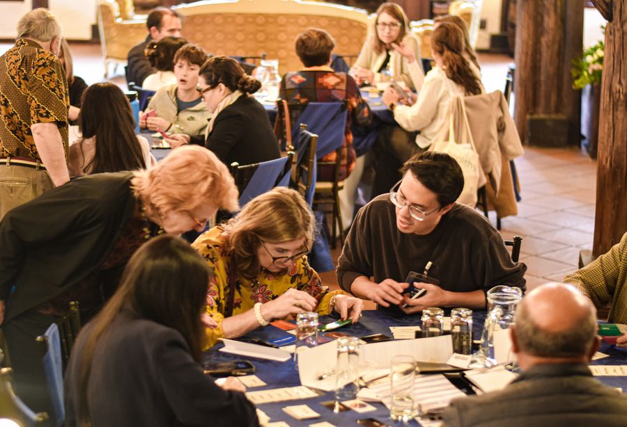 Guests playing a card-based team-building game at round blue-draped tables in a rustic hall