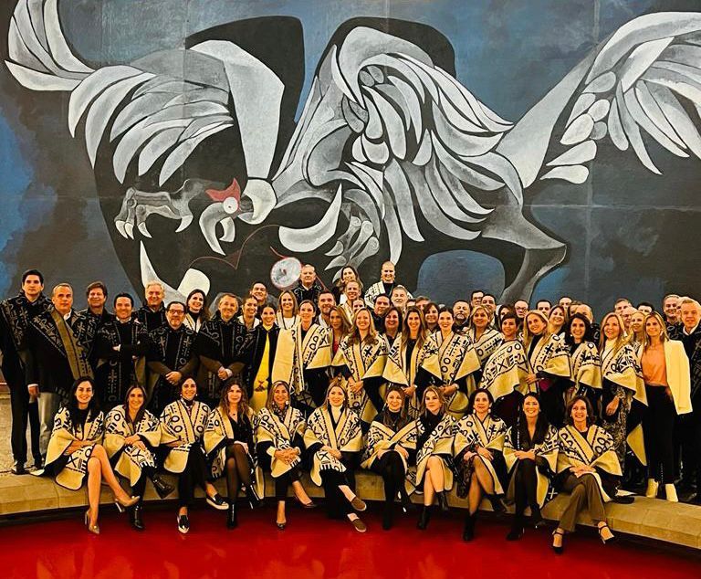 Large corporate group wearing traditional ponchos poses before a giant condor mural