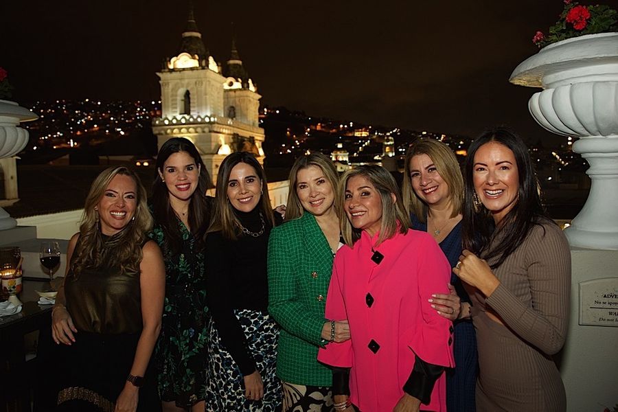 Smiling women pose on a terrace at night with an illuminated colonial church behind