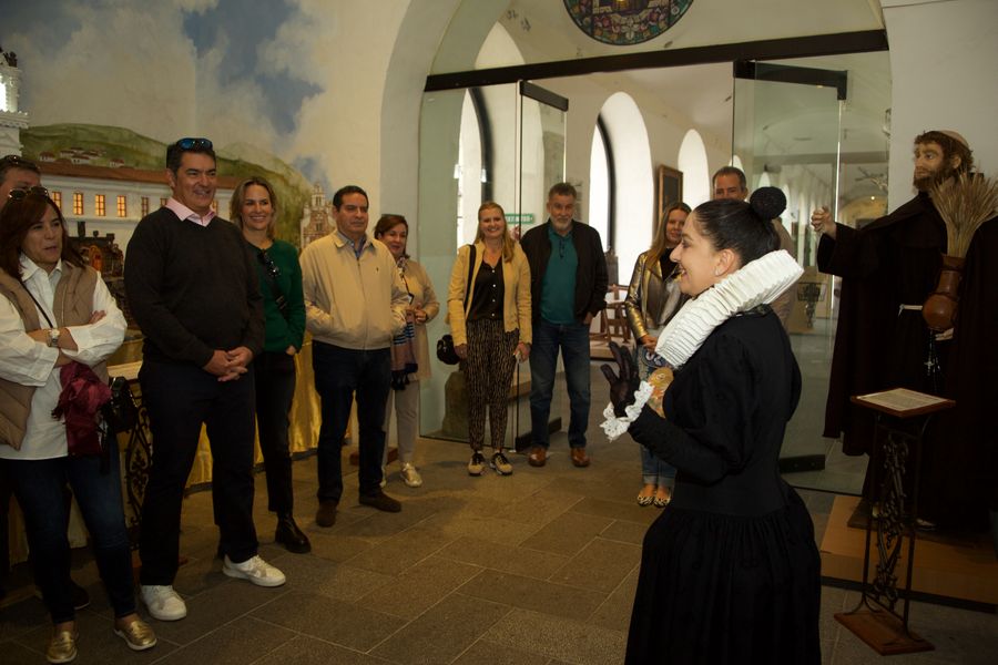 Actress in colonial costume with ruff collar entertains a tour group inside a museum