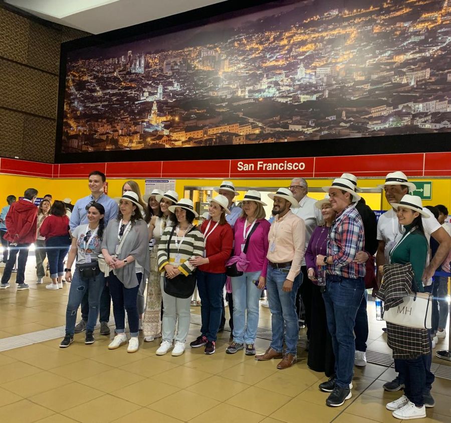 Tour group in Panama hats posing at a Quito metro station below a night city mural