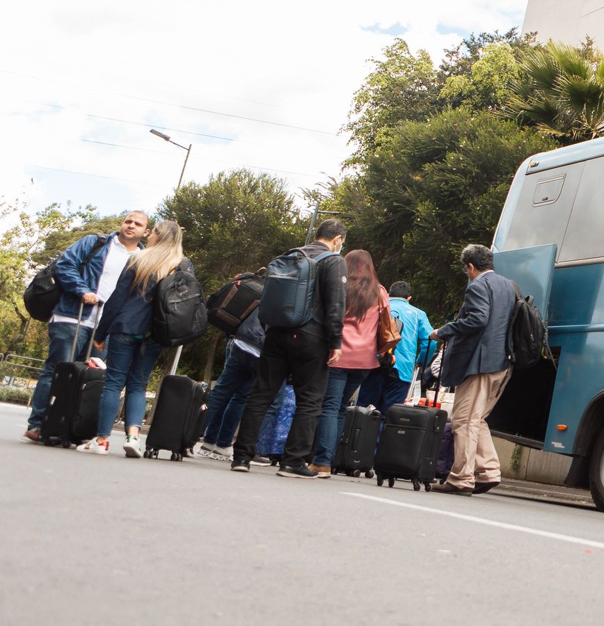Group of travelers with rolling suitcases lining up to board a coach outside a hotel