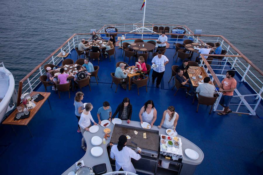 Guests enjoying an open-air dinner on the top deck of a Galápagos cruise ship