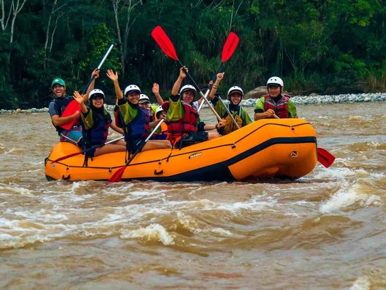 A corporate group whitewater rafting with paddles raised in celebration